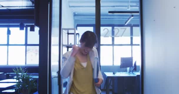 Vue de face d'une entreprise féminine asiatique marche créative dans le couloir d'un bureau moderne, sautant et célébrant le succès, portant un dossier 