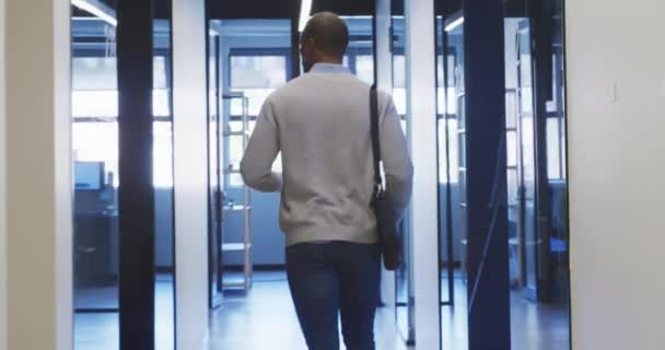 Vue arrière d'une entreprise afro-américaine masculine créative marchant dans le couloir d'un bureau moderne, arrivant dans son bureau 