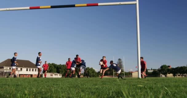 チームストリップを身に着けているラグビー選手の2つの10代の多民族男性チームのフロントビュー スローモーションでプレーフィールド上のラグビー試合中に試合を得点アクションで — ストック動画