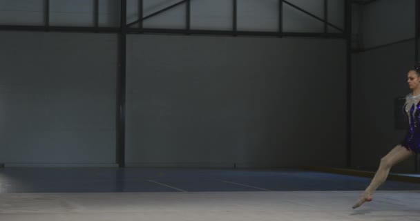 白种人青少年女子体操运动员在体育馆表演的侧视图 她张开双臂跳跃 慢动作时身穿紫色和白色紧身衣 — 图库视频影像