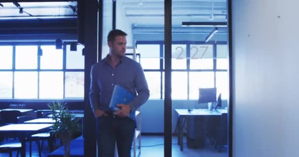 Vue de face d'une entreprise masculine caucasienne marche créative dans le couloir d'un bureau moderne, célébrant le succès, portant un dossier 