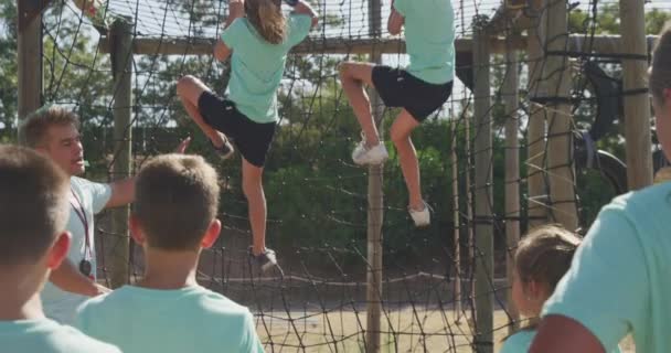 阳光明媚的日子里 一群快乐的白人男孩女孩和一个白人男教练坐在新兵训练营里 穿着绿色T恤 慢吞吞地爬上铁网 — 图库视频影像
