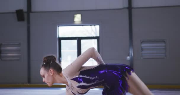 一名专注的年轻白人女子体操运动员在体育馆表演 一边做手推车 慢动作身穿紫色和白色紧身衣的镜头前 — 图库视频影像