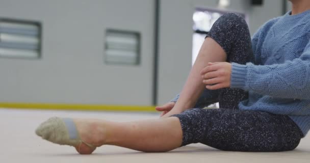 10代の白人女性の体操選手がジムで練習し 床に座って足を伸ばし ウォーミングアップしている様子 スローモーションでの競争のための体操トレーニングハード — ストック動画