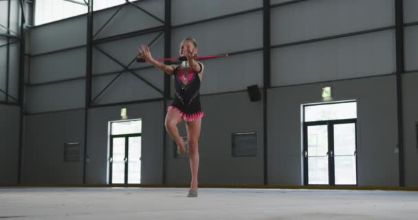关注青少年白种人女体操运动员在体育馆表演 用棍棒锻炼 慢动作穿着黑色和粉色紧身衣的前景 — 图库视频影像