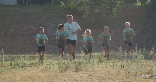 在阳光灿烂的日子里 一群快乐的白人男孩女孩和一个白人男子教练在新兵训练营一起 身穿绿色T恤衫 慢吞吞地奔跑着 — 图库视频影像