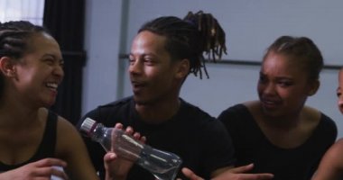 Parlak bir stüdyoda dans kursu sırasında siyah kıyafetler giyen, dans eğitimi alan, mola veren, su içen ve ağır çekimde konuşan çok ırklı kadın ve erkek modern dansçılardan oluşan bir grup.