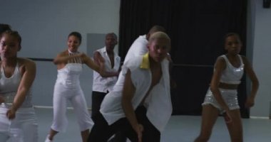 Parlak bir stüdyoda dans kursunda dans rutini uygulayan, beyaz kıyafetler giyen ve hareketlerini yavaş çekimde senkronize eden çok ırklı kadın ve erkek modern dansçılar.