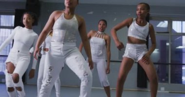 Bir grup melez modern dansçı beyaz kıyafetler giyip dans kursunda hareketlerini senkronize ederek dans ediyorlar.