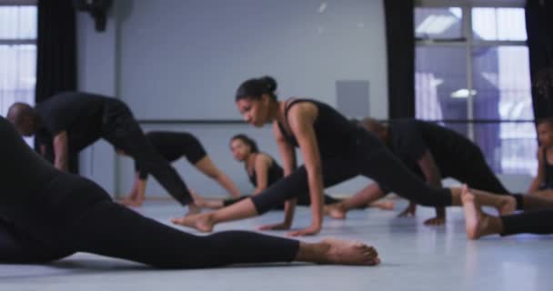 明るいスタジオでダンスクラス中にダンスルーチンを練習黒の衣装を身に着けているフィットの男性と女性の現代ダンサーの多民族グループ 床に横たわって ストレッチ スローモーションで — ストック動画