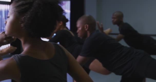 Groupe multi-ethnique de danseurs modernes hommes et femmes en forme portant des tenues noires pratiquant une routine de danse lors d'un cours de danse dans un studio lumineux, faisant une pose et la maintenant immobile, au ralenti 