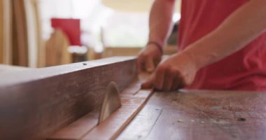 Kafkas erkek sörf tahtası yapımcısı stüdyosunda çalışıyor, kulaklık takıyor, tezgahın arkasında duruyor ve bir sörf tahtası projesi hazırlıyor, ahşabı kesiyor, ağır çekimde.