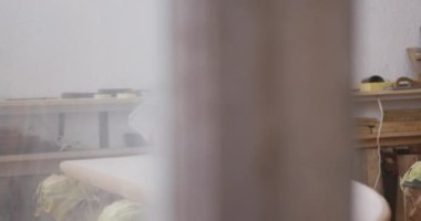 Beyaz erkek sörf tahtası yapımcısı, uzun sarı saçlı, yüz maskesi takan, stüdyosunda çalışan, sörf tahtasını yavaş çekimde cilalayan.