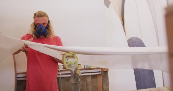 白人男性サーフボードメーカー呼吸面マスクを着用し 彼のスタジオで働いて スローモーションで白い布を切断 — ストック動画