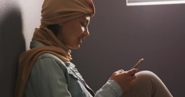 베이지 히잡을 계단에 스마트폰을 평상복을 동작으로 아시아 여학생의 모습을 클로즈업 — 비디오