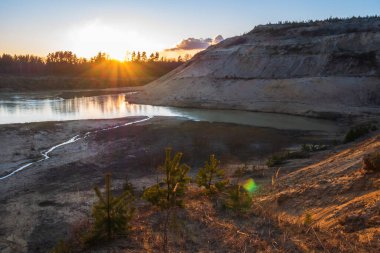 Terk edilmiş bir taş ocağının arka planında gün batımı.