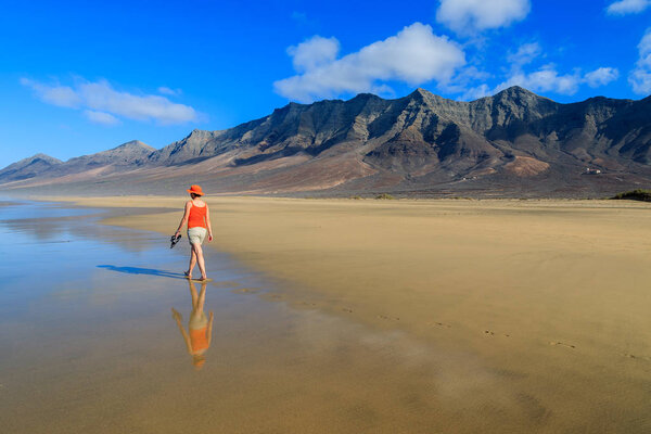Young woman tourist walking on Cofete beach and volcanic mountains in the background on Jandia peninsula, Fuerteventura, Canary Islands, Spain
