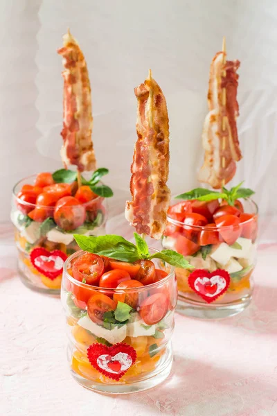 Festive caprese salad with fried bacon on skewers in glasses