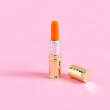 Tüp ruj ve mini havuç pastel pembe bir arka plan üzerinde. Minimalist tarzı. Renk ve şekil yaratıcı bir fikir. Gıda ve moda Tema fanteziler