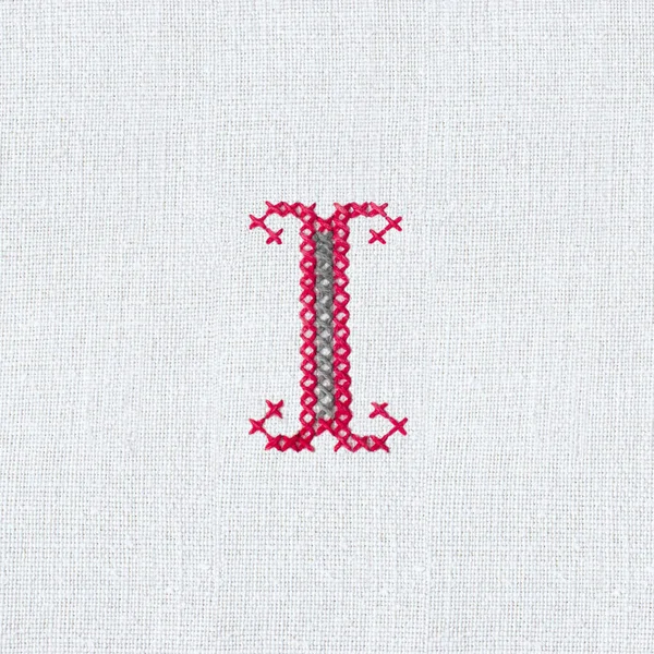 Vintage cross-stitch letter I on linen homespun fabric. Embroidered letter I close-up. Handmade art