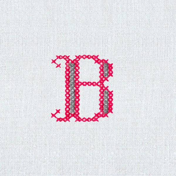 Vintage cross-stitch letter B on linen homespun fabric. Embroidered letter B close-up. Handmade art