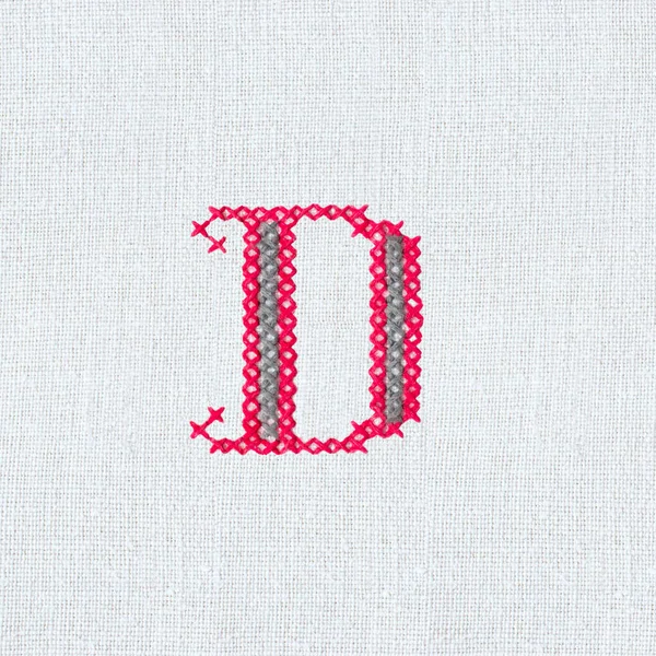 Vintage cross-stitch letter D on linen homespun fabric. Embroidered letter D close-up. Handmade art