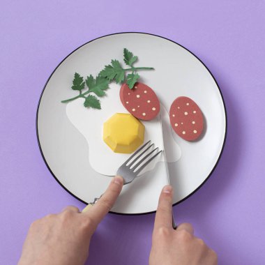 Çatallı ve bıçaklı eller sosisli kızarmış kâğıt yumurtayı keser. Gerçekçi el yapımı kağıt objeler. Kağıt sanat ve zanaat. En az sanat yemeği konsepti. Kare resim