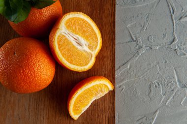 Bütün ve yeşil yapraklı portakal dilimleri beyaz bir zemin üzerinde tahta bir tahtanın üzerinde yatıyor. Yukarıdan bakan parlak portakallar. Yakın çekim ve üst görüntü, düz çizgi. Yaz havası ve sabah kahvaltısı