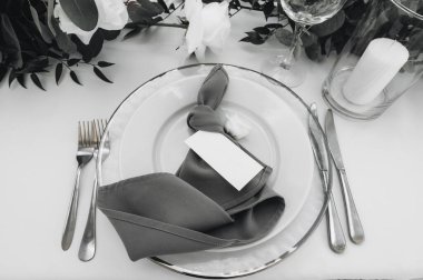 Beyaz bir masa örtüsünün üzerinde çatal ve bıçağın yanında yazı plakası olan bir tabak. Düz yatıyordu