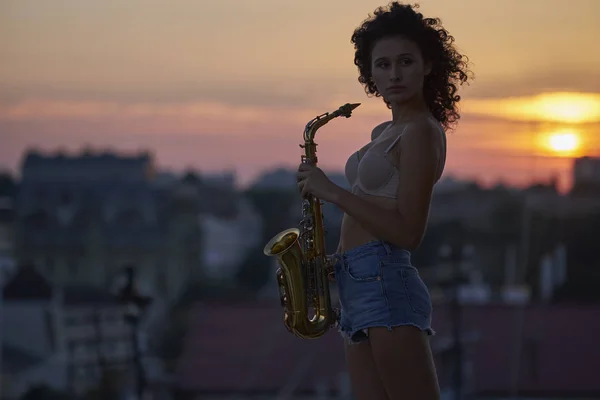 Молодая девушка с саксофоном на крыше Стоковая Картинка