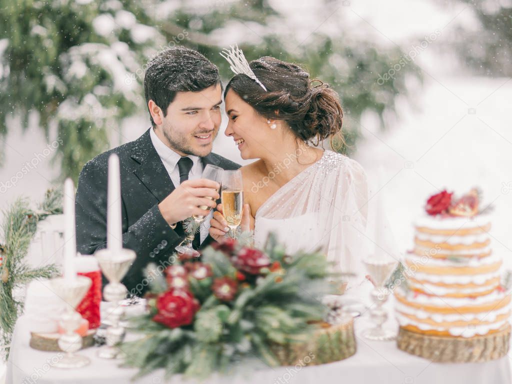 Winter wedding outdoor. Beautiful couple drinking champagne, smiling and kissing