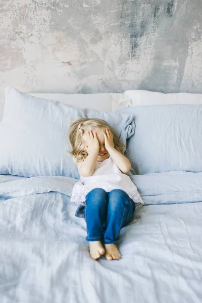 beautiful little blonde girl closed eyes by hands in bed at home