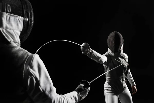 ヘルメットとフェンシングの黒の背景に白のユニフォームを身に着けている 人の女性 — ストック写真