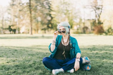 Yeşil park yeşil çimenlerin üzerinde oturan oturan genç boho kadın