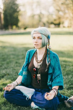 Park yeşil çimenlerin üzerinde oturup meditasyon mavi saçlı genç hippi kadını