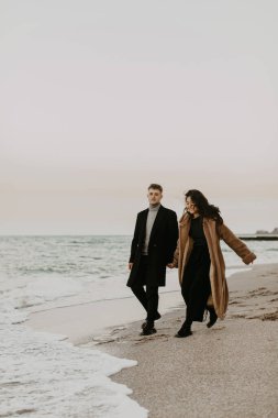 Birbirlerine aşık genç bir çift deniz kenarında yürüyor, eğleniyorlar.