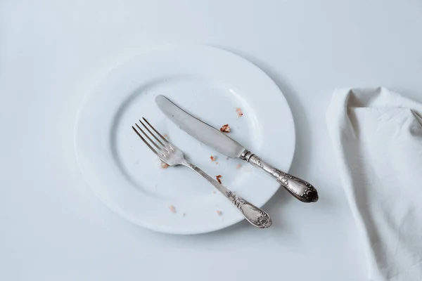 Piatto bianco con forchetta, coltello e stropicciato su fondo bianco — Foto Stock