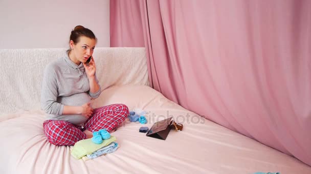 Щаслива вагітна жінка телефонує на смартфон, сидячи в ліжку в спальні — стокове відео