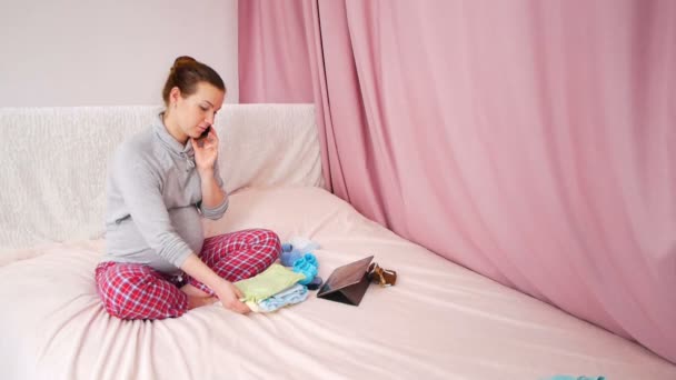 Mujer embarazada feliz llamando en el teléfono inteligente mientras está sentado en la cama en el dormitorio — Vídeos de Stock