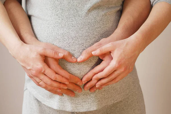 Happy young couple showing heart on belly of pregnant wife — Stock Photo, Image