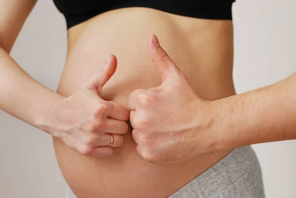 Happy young parents showing OK sign on pregnant wife belly Stock Photo