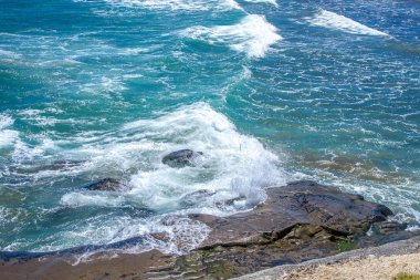 Taşlı bir sahilde dalgalar kopuyor.