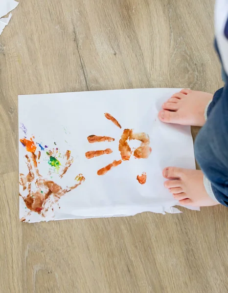 Child standing on paper with color handprints — Stock Photo, Image