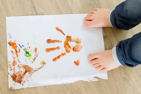 Lapsi seisoo paperilla värillinen kädenjäljet — kuvapankkivalokuva