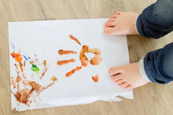 Child standing on paper with color handprints — Stock Photo, Image