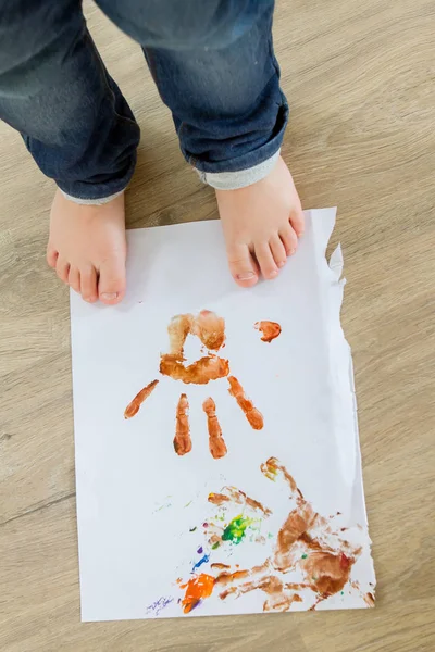 Child standing on paper with color handprints — Stock Photo, Image