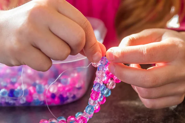 Giovane ragazza bambino facendo braccialetto di perle — Foto Stock