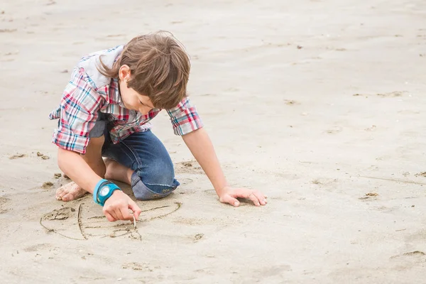 Молодий хлопчик малює в піску — стокове фото