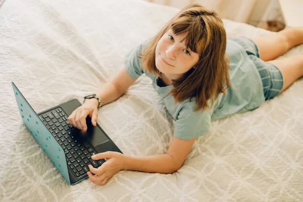 家のベッドの上に寝そべっているラップトップを持つ子供の女の子の屋内カジュアルポートレート — ストック写真