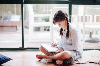 Pencere kenarındaki evde yazan küçük kızın kapalı bir portresi.